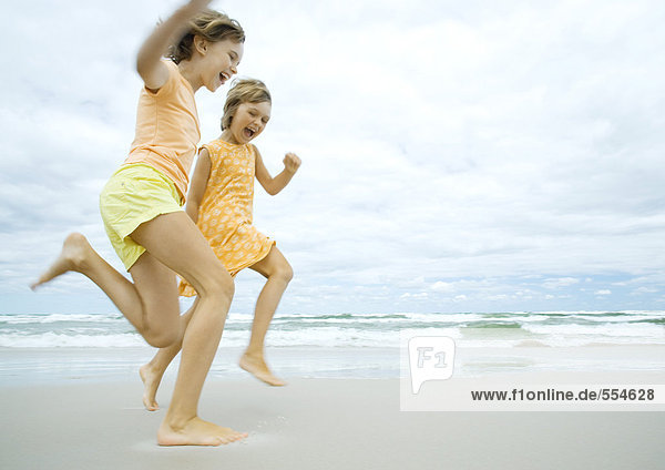 Zwei Mädchen laufen barfuß am Strand  Seitenansicht