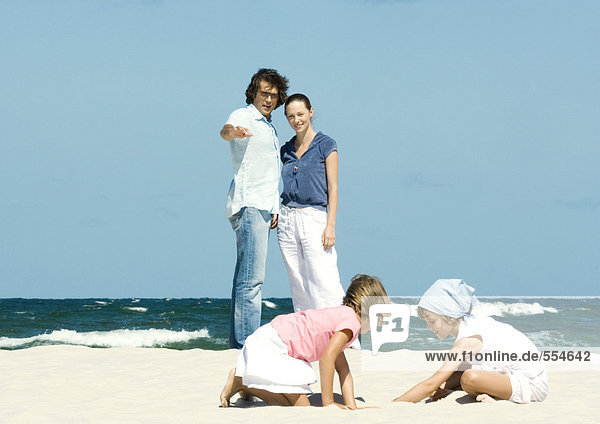 Familie am Strand  Eltern beobachten Töchter beim Spielen im Sand