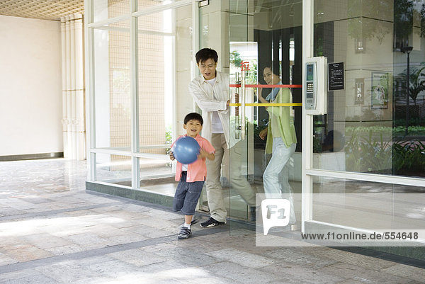 Family exiting apartment building lobby  boy carrying ball