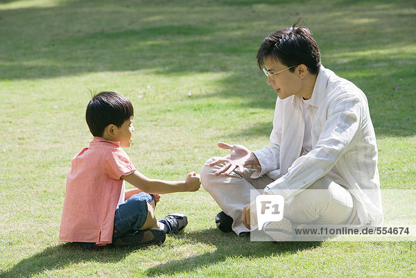 'Father and son sitting on grass playing ''rock paper scissors'''