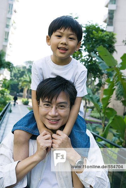 Boy riding on father's shoulders  front view  smiling at camera