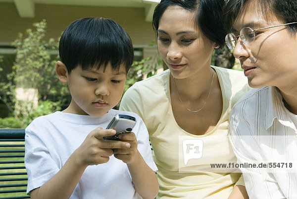 Familie  Junge  der das Handy benutzt  während die Eltern zusehen.