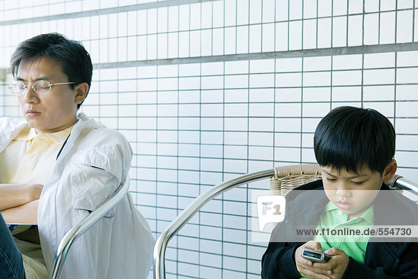 Junge benutzt Handy  während Vater mit geschlossenen Augen sitzt.