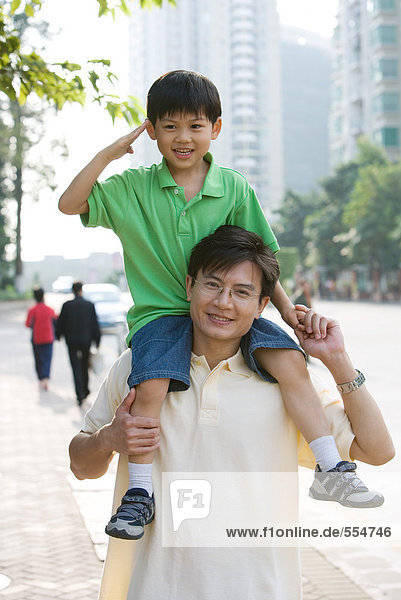 Boy riding on father's shoulders  saluting camera