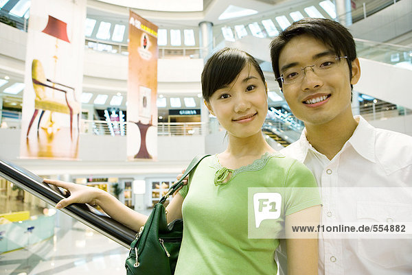 Couple taking escalator in shopping mall  smiling at camera