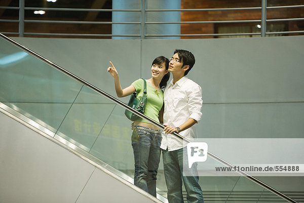 Couple taking escalator in shopping mall  woman pointing out of frame