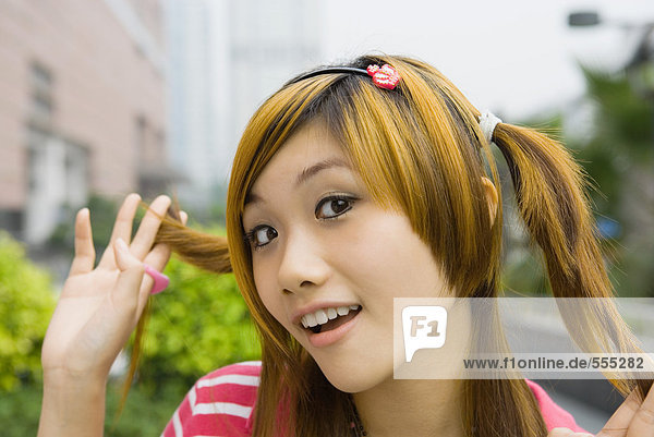 Teenage girl holding pigtail  looking at camera  portrait
