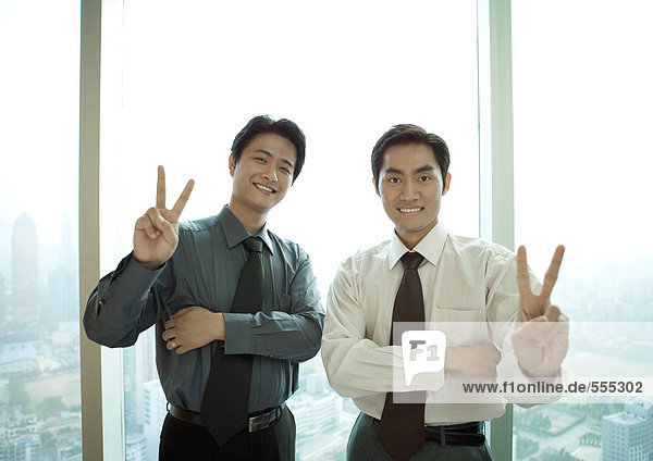 Zwei Geschäftsleute  die ein Siegeszeichen machen  lächelnd vor der Kamera.