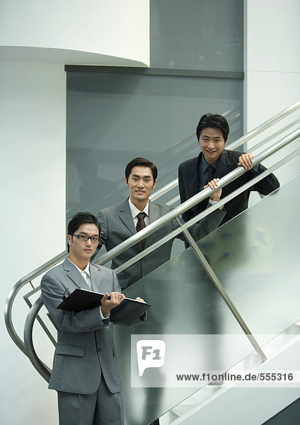 Drei Geschäftsleute stehen an der Treppe und schauen in die Kamera.