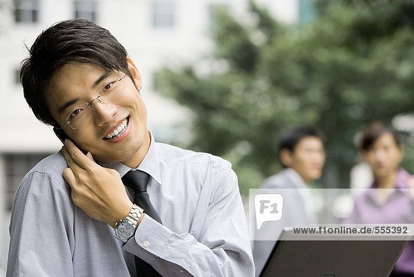Junger Geschäftsmann hält Handy gegen die Schulter  lächelt in die Kamera