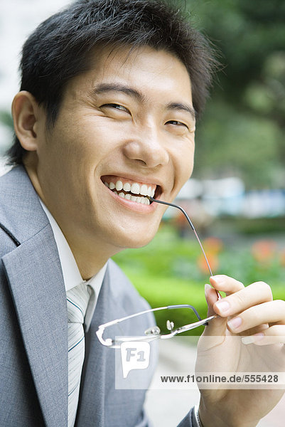 Businessman holding glasses up to mouth  smiling at camera  portrait