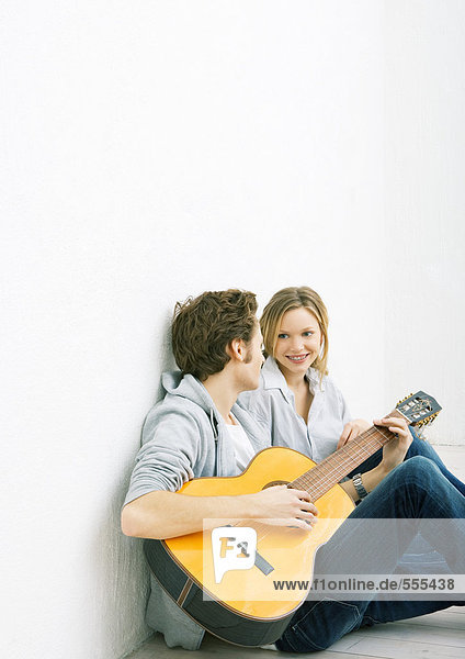 Young man and woman sitting on ground  man playing guitar