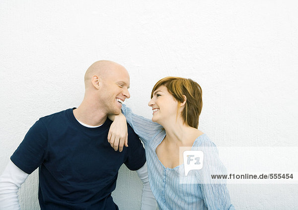 Junges Paar lächelt sich an  von Angesicht zu Angesicht  Frau mit Ellenbogen auf der Schulter des Mannes.