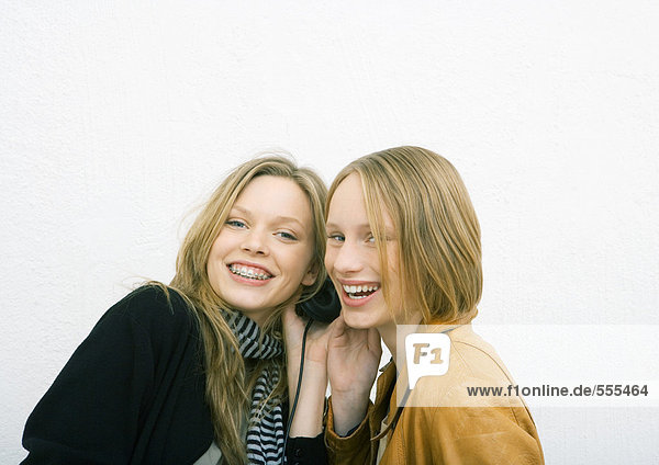 Two young female friends sharing headphones  smiling at camera