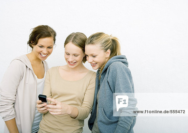 Drei junge Freundinnen  die zusammen auf das Handy schauen  lächelnd