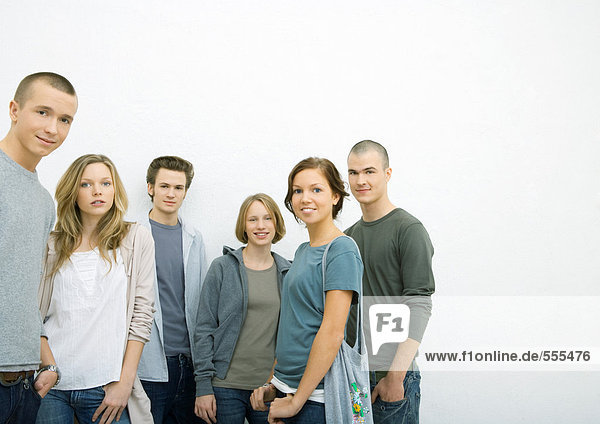 Group of young adults standing with hands in pockets  smiling at camera