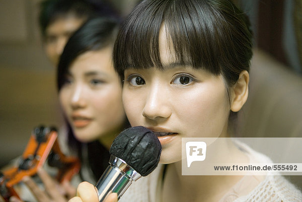 Junge Frau hält Mikrofon in Karaoke-Bar  Nahaufnahme  Freunde im Hintergrund