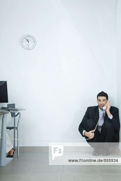 Businessman sitting on floor  in corner  talking on phone