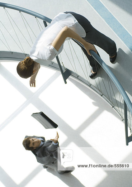 Businessman throwing briefcase up to woman from lower floor  full length  high angle view