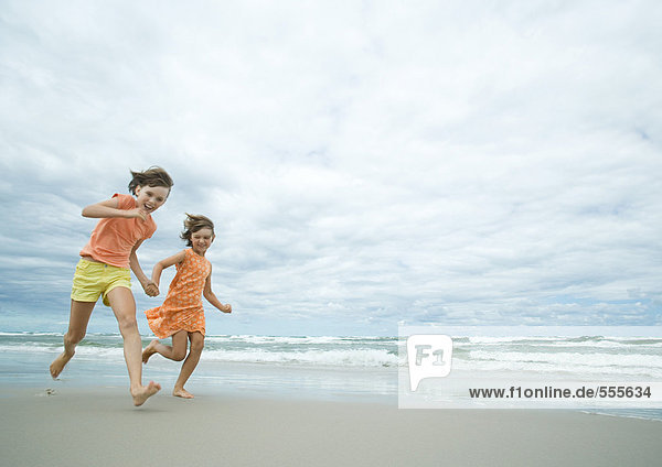 Two girls running hand in hand on beach  full length