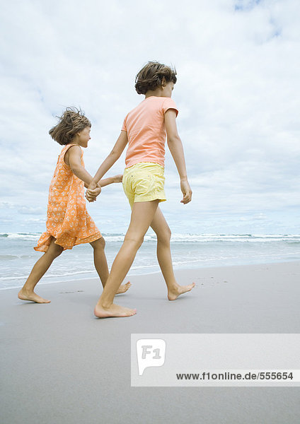 Zwei Mädchen gehen  halten sich an den Händen  am Strand.