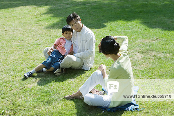 Family sitting on grass  woman taking photo of man and boy