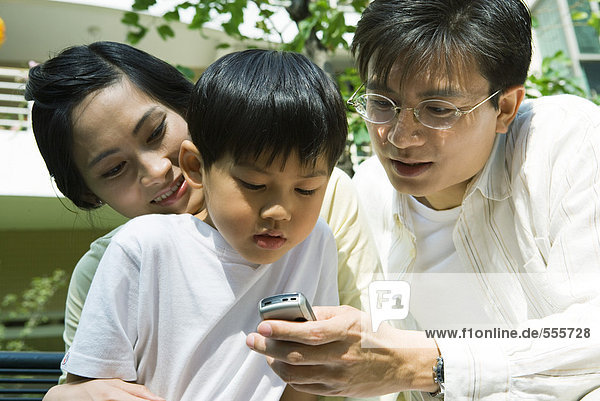 Boy with mother and father  father holding out cell phone for boy to see