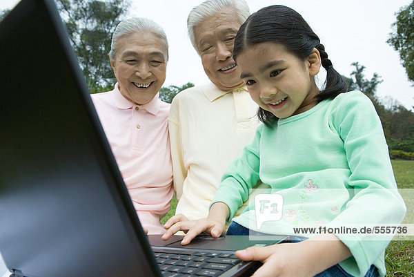 Mädchen mit Laptop  während Großeltern zuschauen