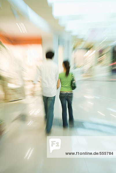 Couple walking through shopping mall  rear view  full length
