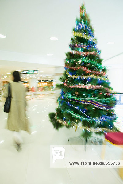 Shopperin geht am Weihnachtsbaum in der Mall vorbei