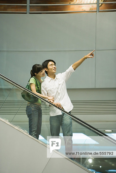 Paar auf Rolltreppe  Mann zeigt auf