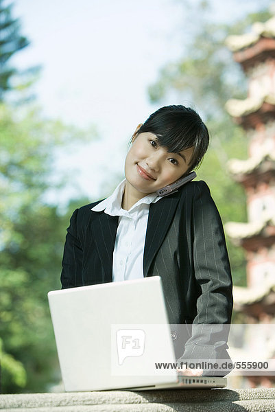 Woman using laptop and cell phone  pagoda in background