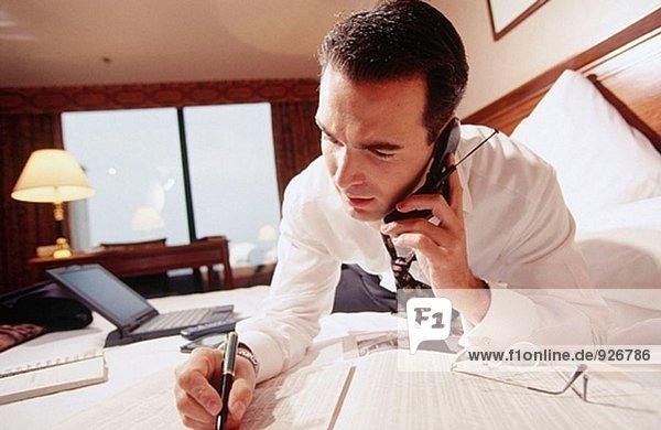 Businessman working on the bedon the bed and talking on cell phone in a hotel room