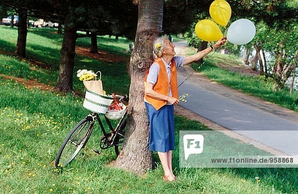 Senior woman with bike and balloons in park