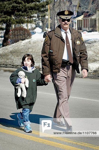 Policeman helps little girl to cross the road.