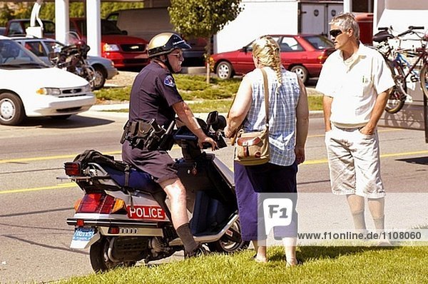 Senior männlichen Polizeibeamten auf einem Motorrad spricht mit adult paar