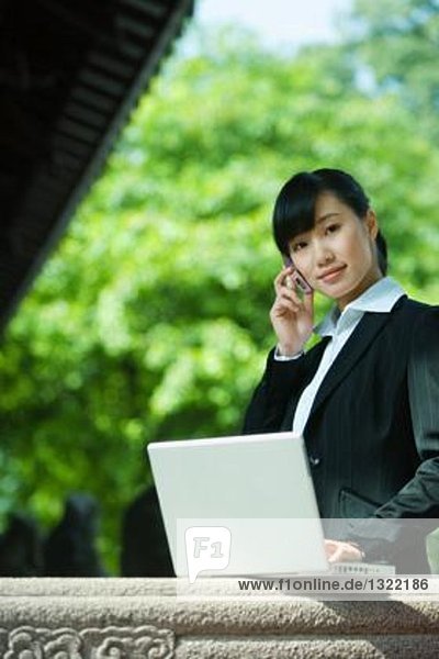 Young woman using laptop and cell phone