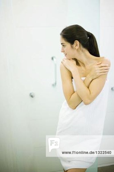 Woman standing wrapped in towel  hands on shoulders  looking away
