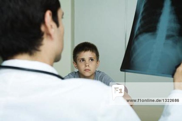 Der Arzt sitzt dem Jungen gegenüber und hält das Röntgenbild hoch.