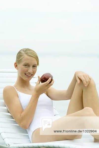 Teenagermädchen im Badeanzug  im Sessel sitzend  Apfel haltend