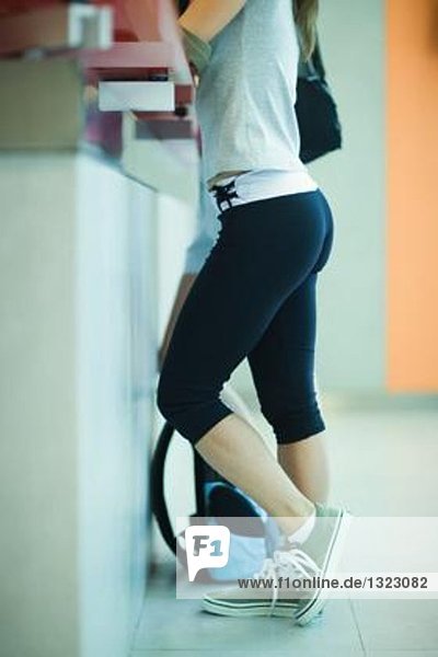 Junge Frau steht am Tresen des Fitnessstudios und schaut durch die Tasche.