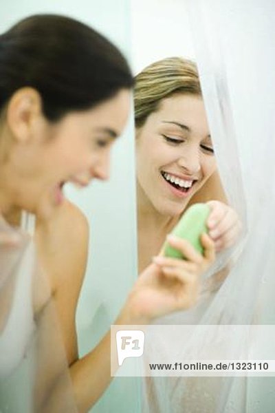 Two young women in showers  one handing bar of soap to the second