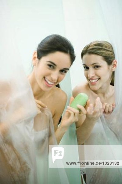 Zwei junge Frauen beim Duschen  eine reicht der anderen ein Stück Seife.