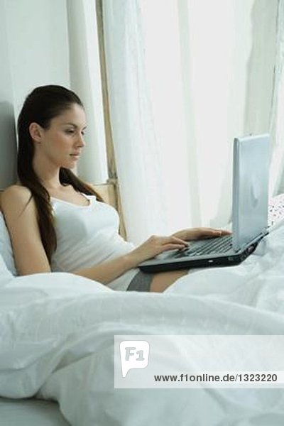 Frau im Bett sitzend  mit Laptop