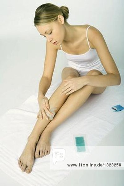 Young woman using wax hair removal product on legs