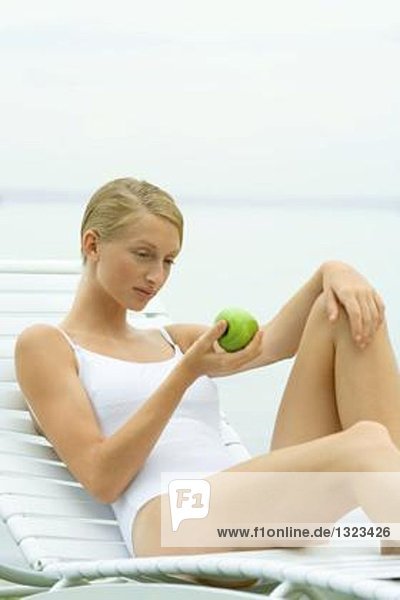 Teenagermädchen im Badeanzug sitzend auf Sessel  Apfel haltend