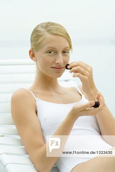Teenage girl in swimsuit sitting on lounge chair  smelling blackberries