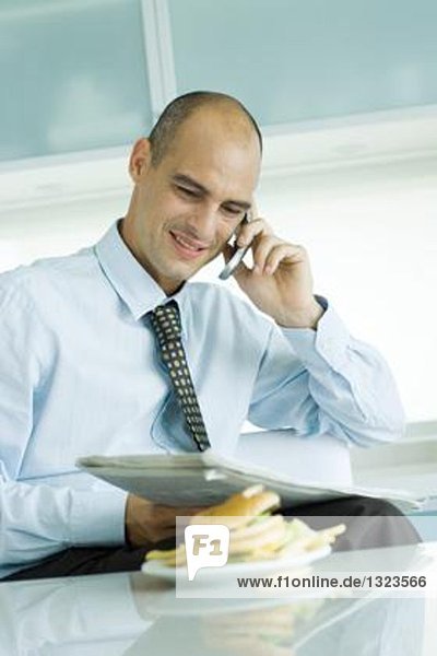 Man using phone and reading newspaper  hamburger on table in foreground