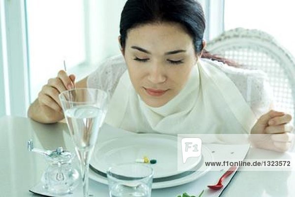 Frau sitzt am gedeckten Tisch  trägt Serviette um den Hals  Vitamine auf dem Teller