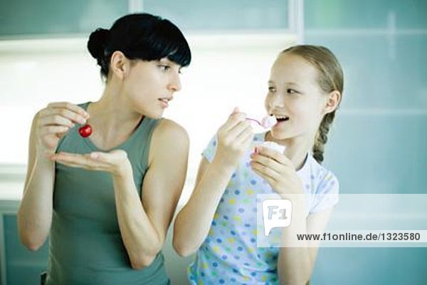 Frau isst Kirsche  beobachtet Mädchen beim Joghurtessen